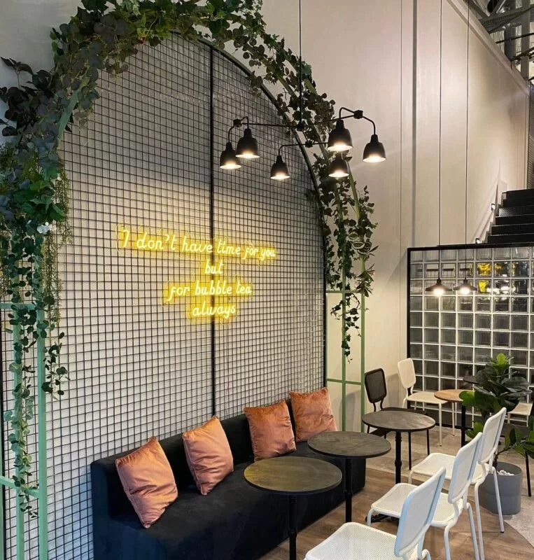 Yellow LED neon lettering on a café wall above green sofas
