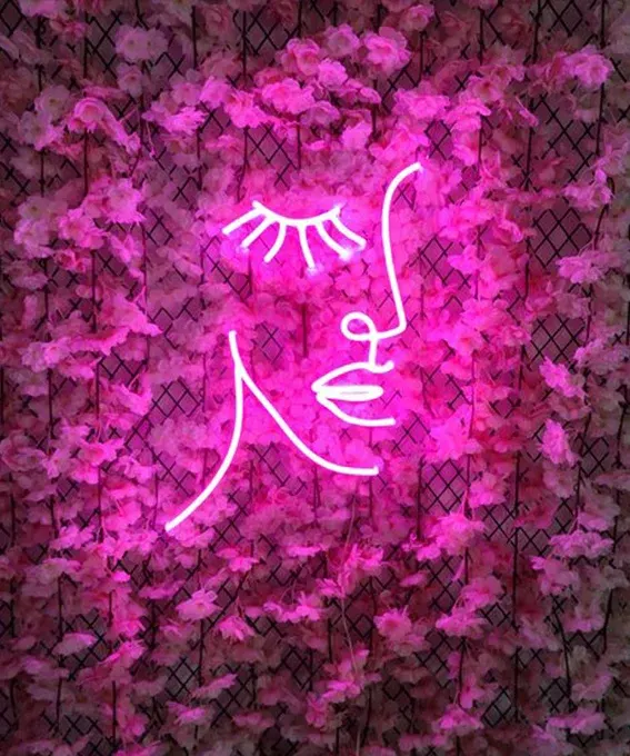 Pink LED neon face line art on a flower wall